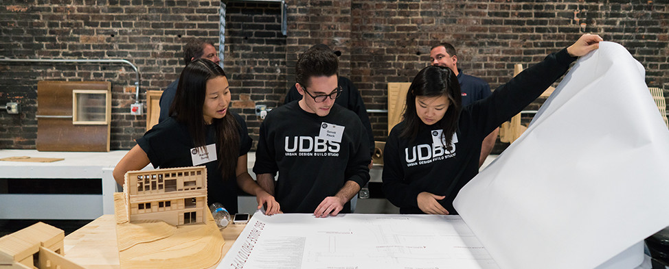 Three students from the Urban Design Build Studio are shown looking through blueprints during the Project RE dedication at Construction Junction.