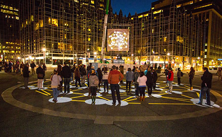 Nighttime image of a group of people interacting with the “Congregation” public art project in Market Square in Downtown Pittsburgh. This work was created by KMA and presented by Market Square Public Art.