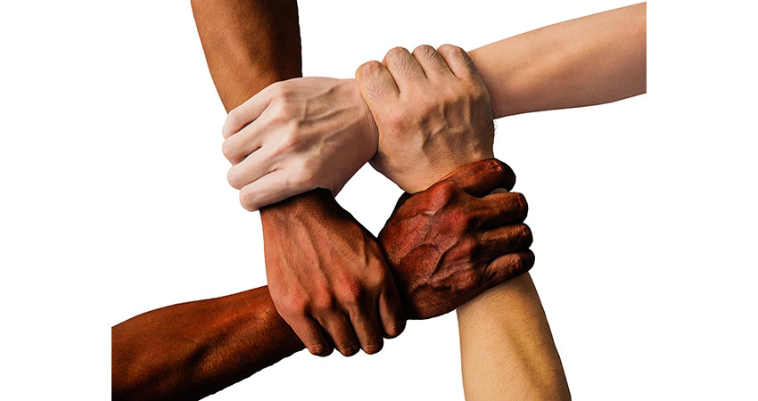Image of the arms of four people of different ethnicities with their arms crossed, grasping each other wrists.